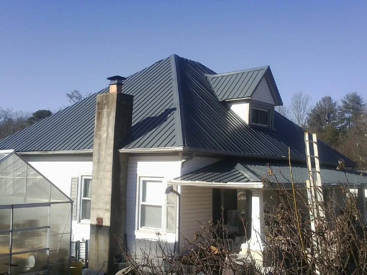 Dark blue standing seam metal roof on a white farmhouse with dormer — Slate & Tile Roof Repair by Roofing Brothers in Ashippun