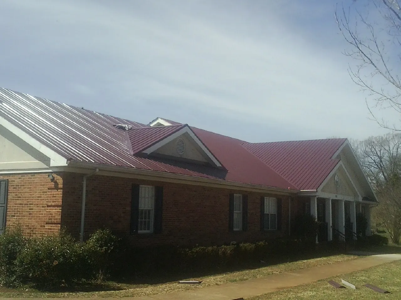 Red metal roof with gabled entries on a long brick building, from a Hail Damage Roof Repair job in Ashippun