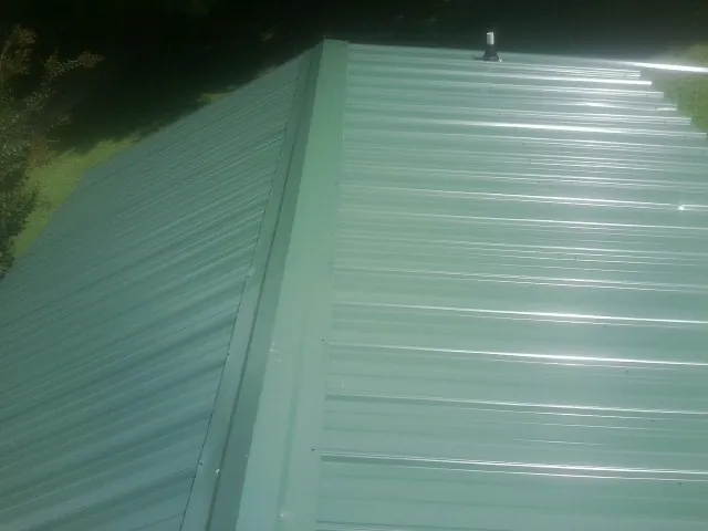 New green metal panels meeting at the ridge of a roof — Flat Roof Repair work by our crew in Ashippun