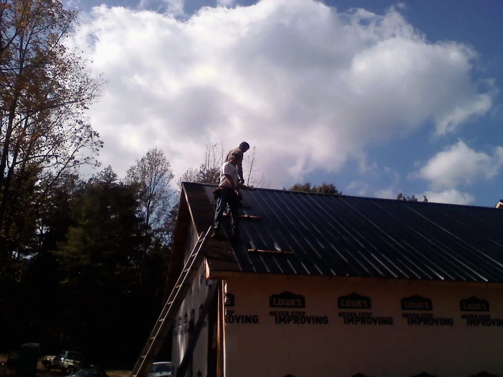 Roofer fastening dark metal panels high against a cloudy sky, from a Roof Inspection job in Ashippun