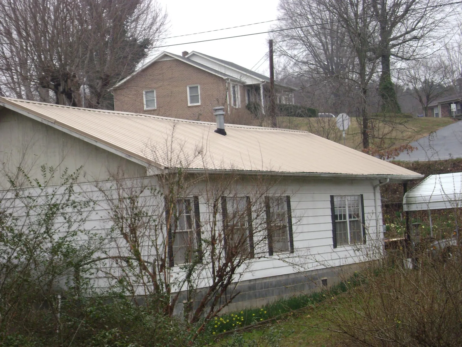Tan metal roof on a white sided house set into a hillside — Commercial Roofing by Roofing Brothers in Ashippun